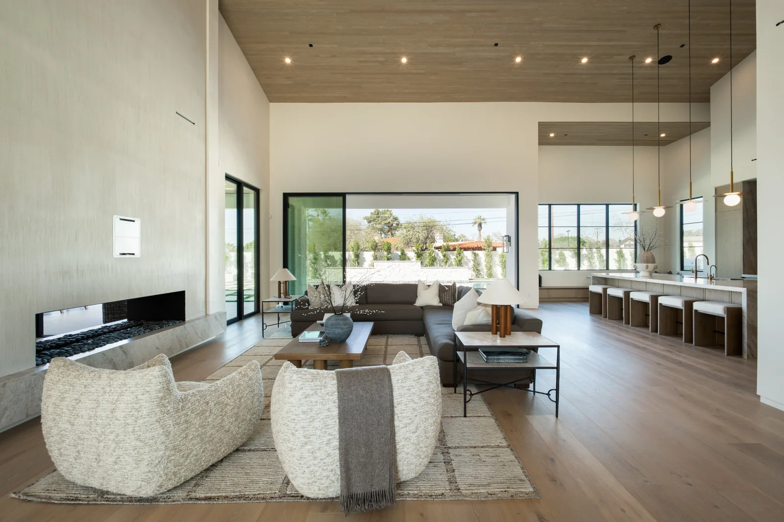 Great room with linear fireplace, beamed ceiling and wall of glass opening to the yard